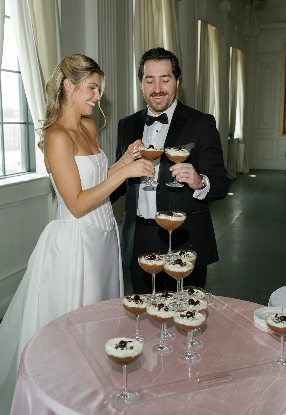 A bride and groom toasting beside a tower of coupe glasses