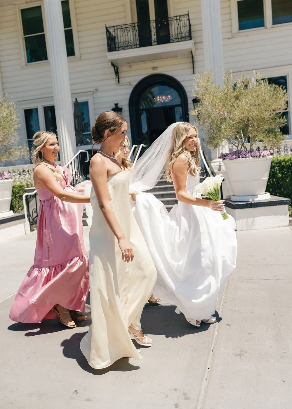 A bride and her bridesmaids carrying her train down the steps of an estate