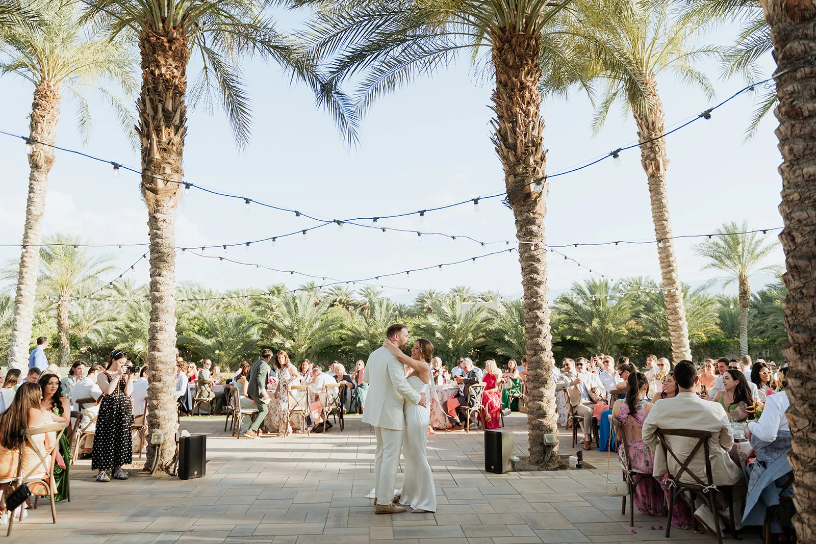 A wedding ceremony under palm trees strung with festoon lights